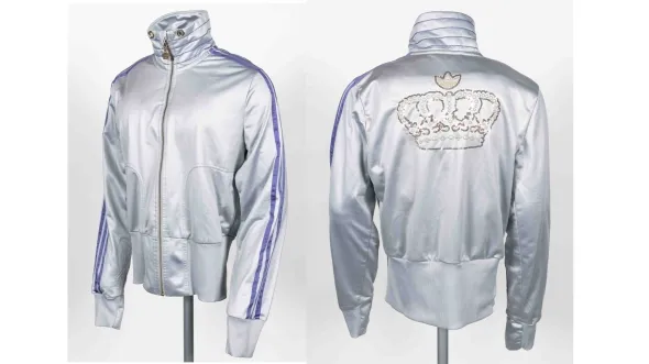 A silver tracksuit jacket with purple racing stripes on the sleeves and an embroidered gold crown on the back