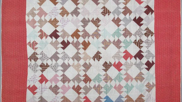 Detail of a quilt with multicolored patterened fabric squares in tones of red and brown on a bias.