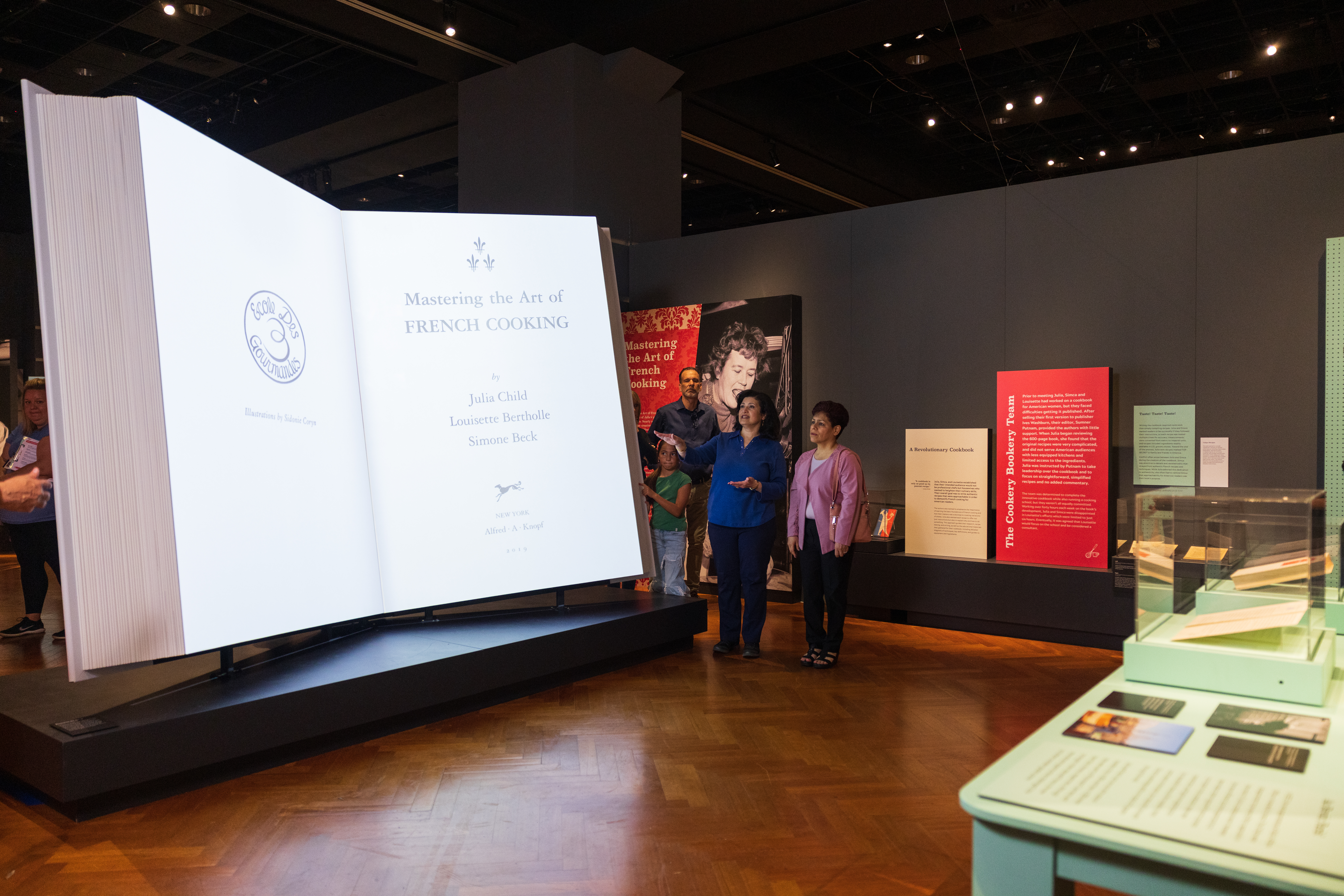 Gallery in Julia Child exhibit showing life size cookbook with people looking on