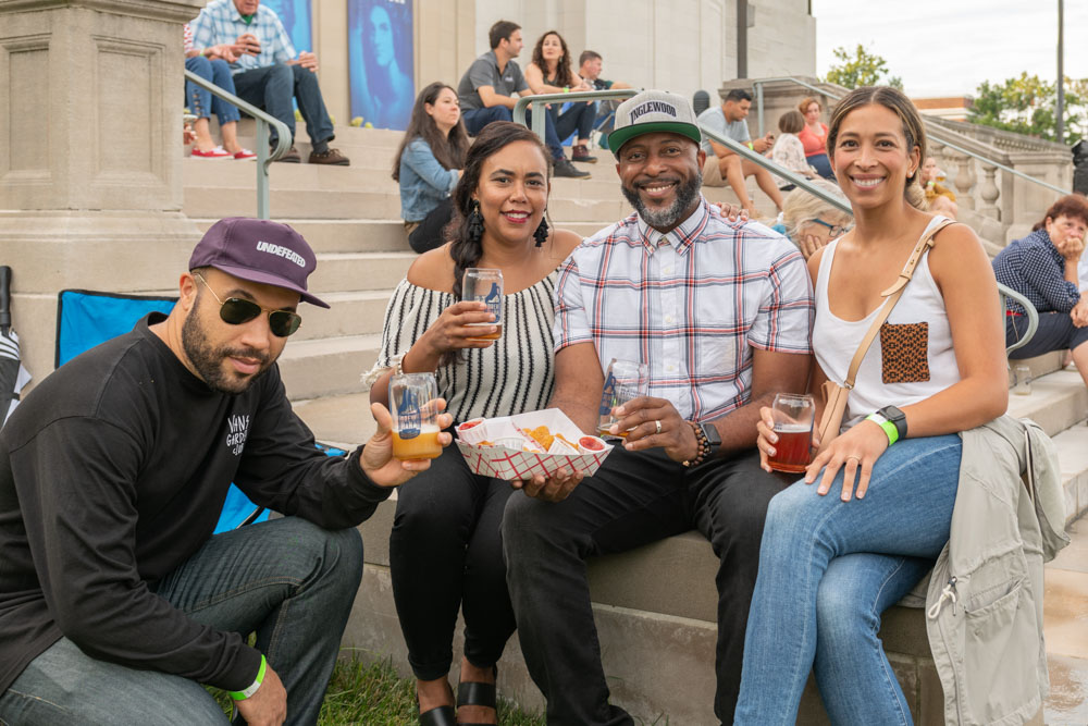 Four people enjoy beer and food on the stone steps of the VMHC