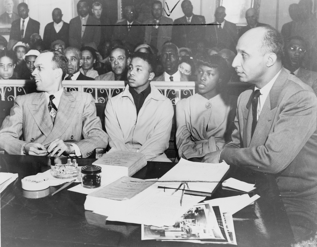 Black and white photograph of Oliver Hill and Spotswood Robinson sitting with students from West Point at a court hearing as other students watch on in the background