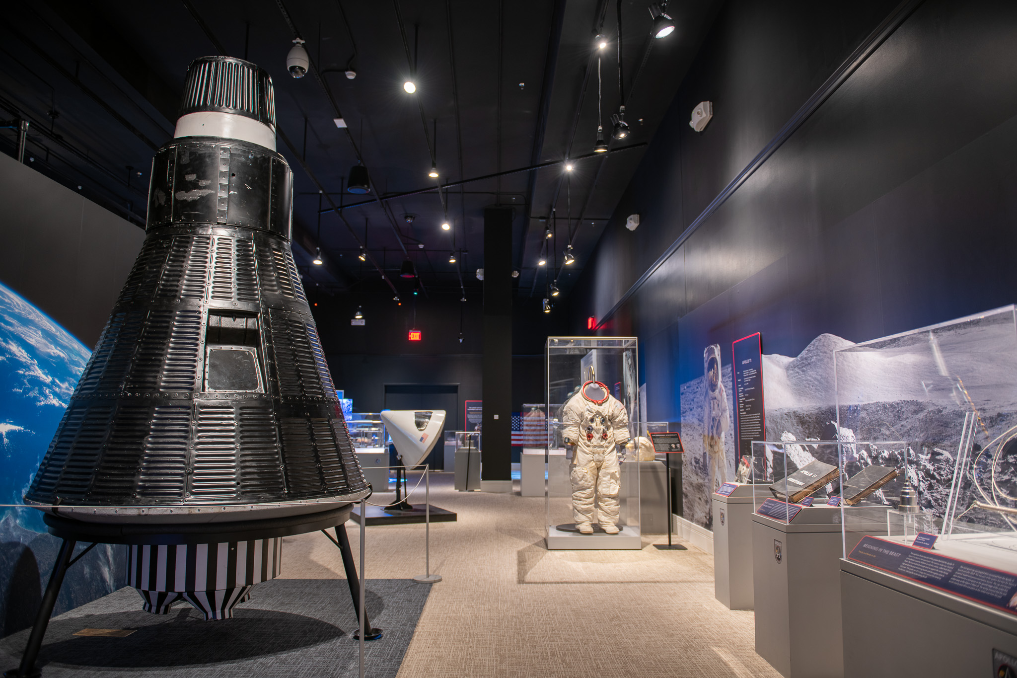 An interior of a gallery with a space capsule, photo of Earth and surface of the moon, and a spacesuit in a display case.