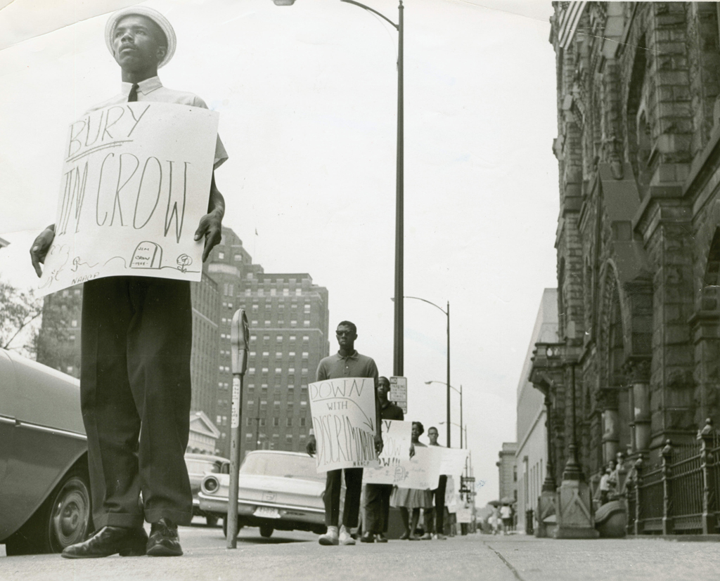Black and white photograph of an African American protestor with sign: "Bury Jim Crow"