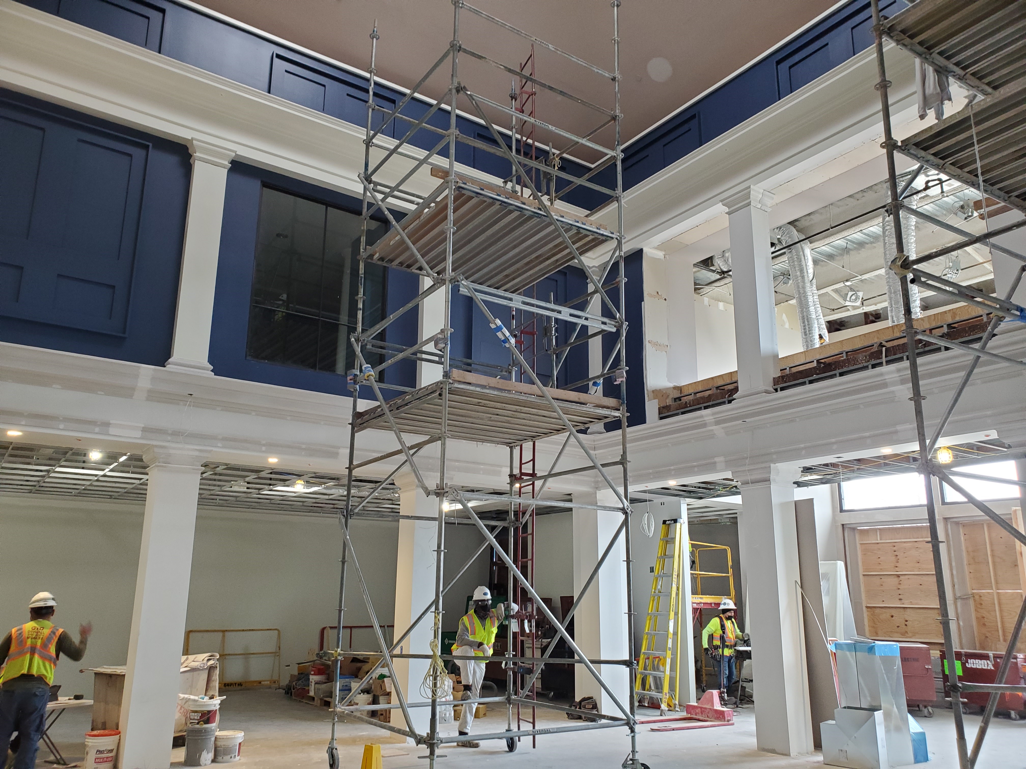 A construction crew uses scaffolding to paint a two-story columned research library with dark blue paint