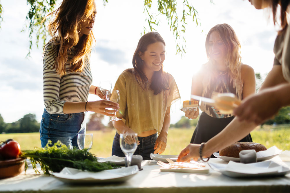 A group of people gather around a table pouring wine.