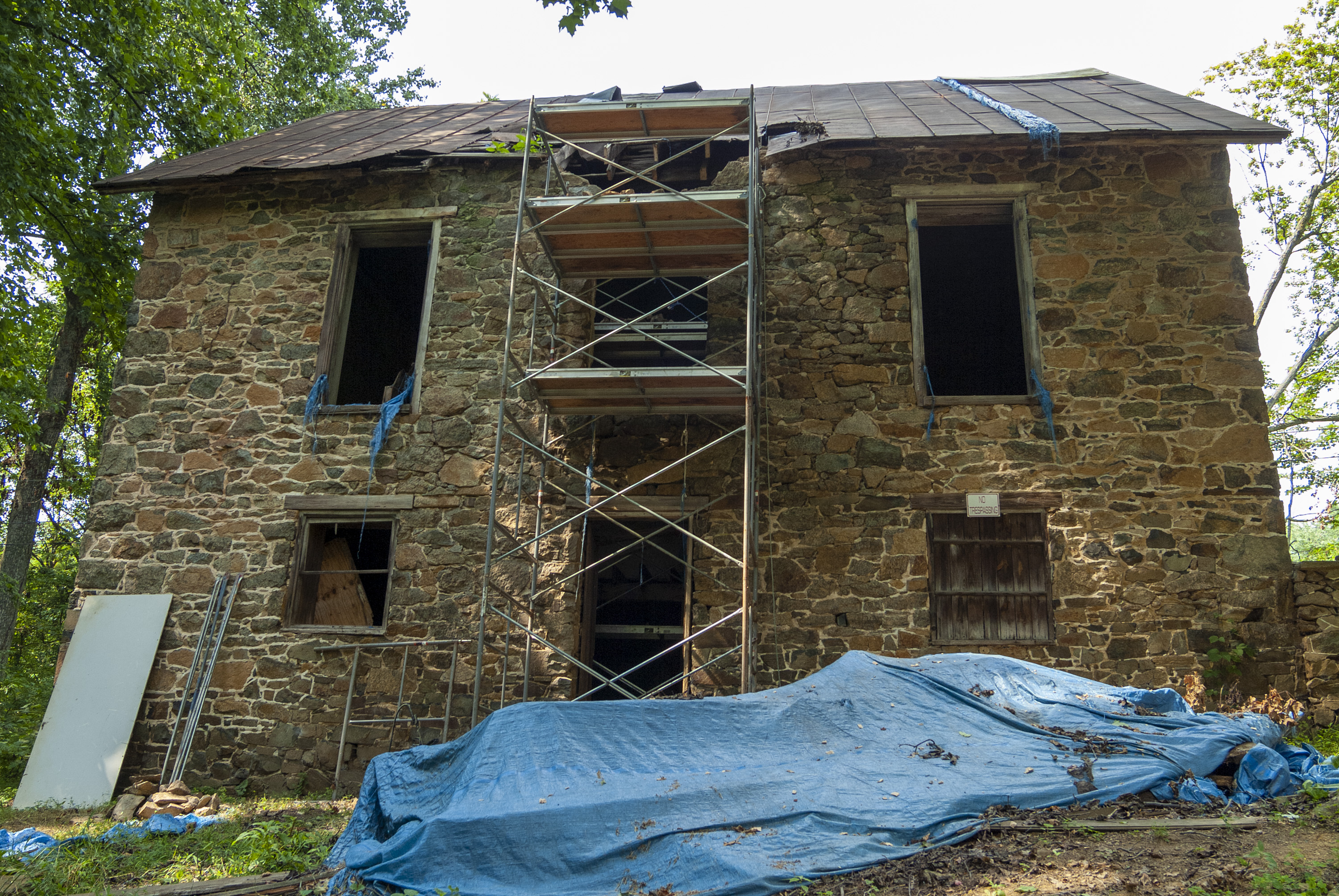 A two-story stone house with scaffolding and tarps on its exterior