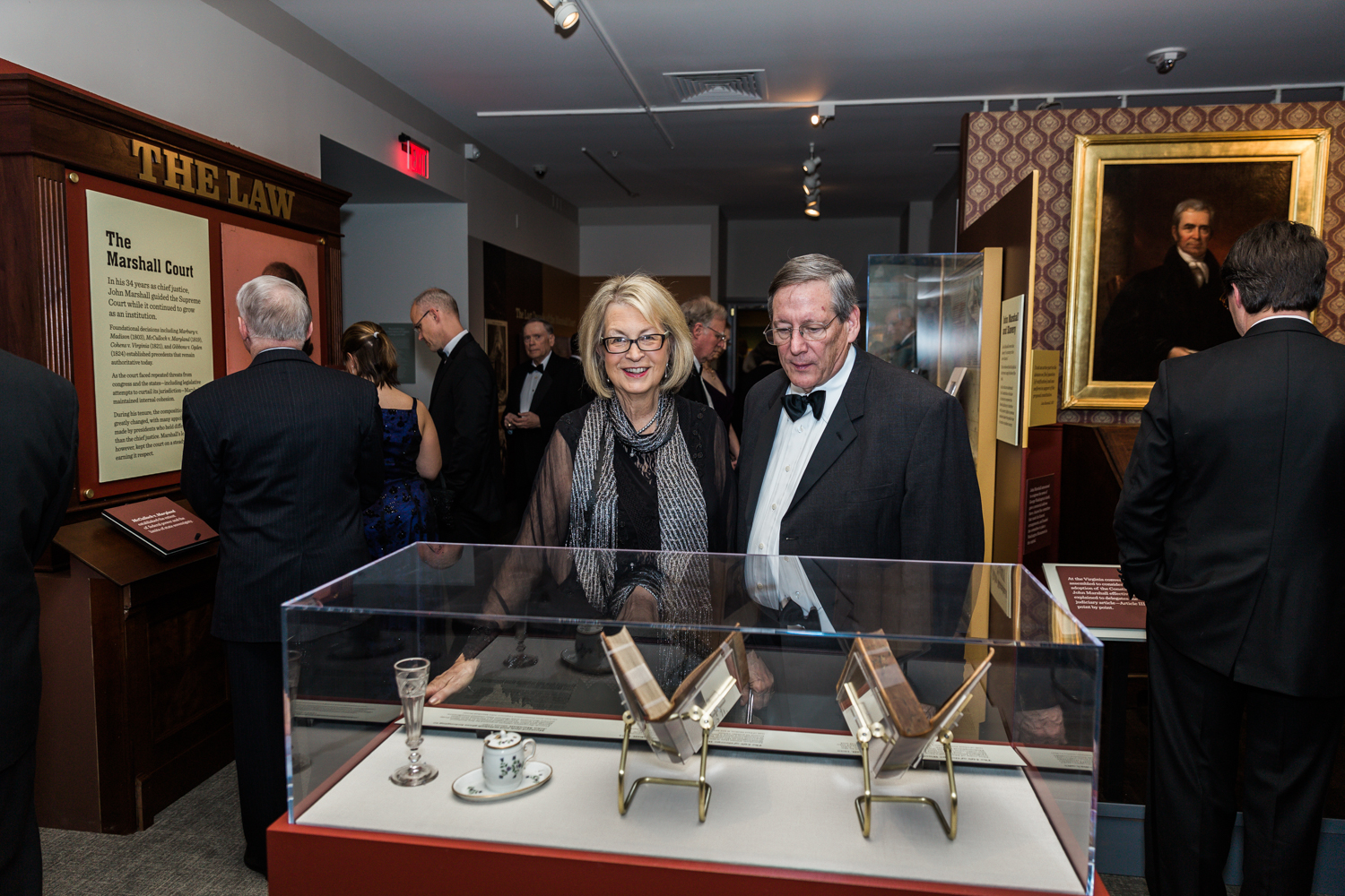 man and woman in formal attire looking at objects in a plexglass case in a museum gallery