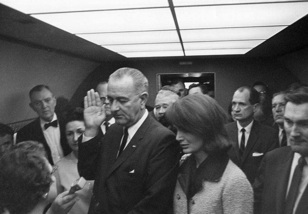 President Lyndon B. Johnson, standing next to First Lady Jacqueline Kennedy, raises his hand as he is sworn in aboard Air Force One, immediately following the death of President John F. Kennedy.