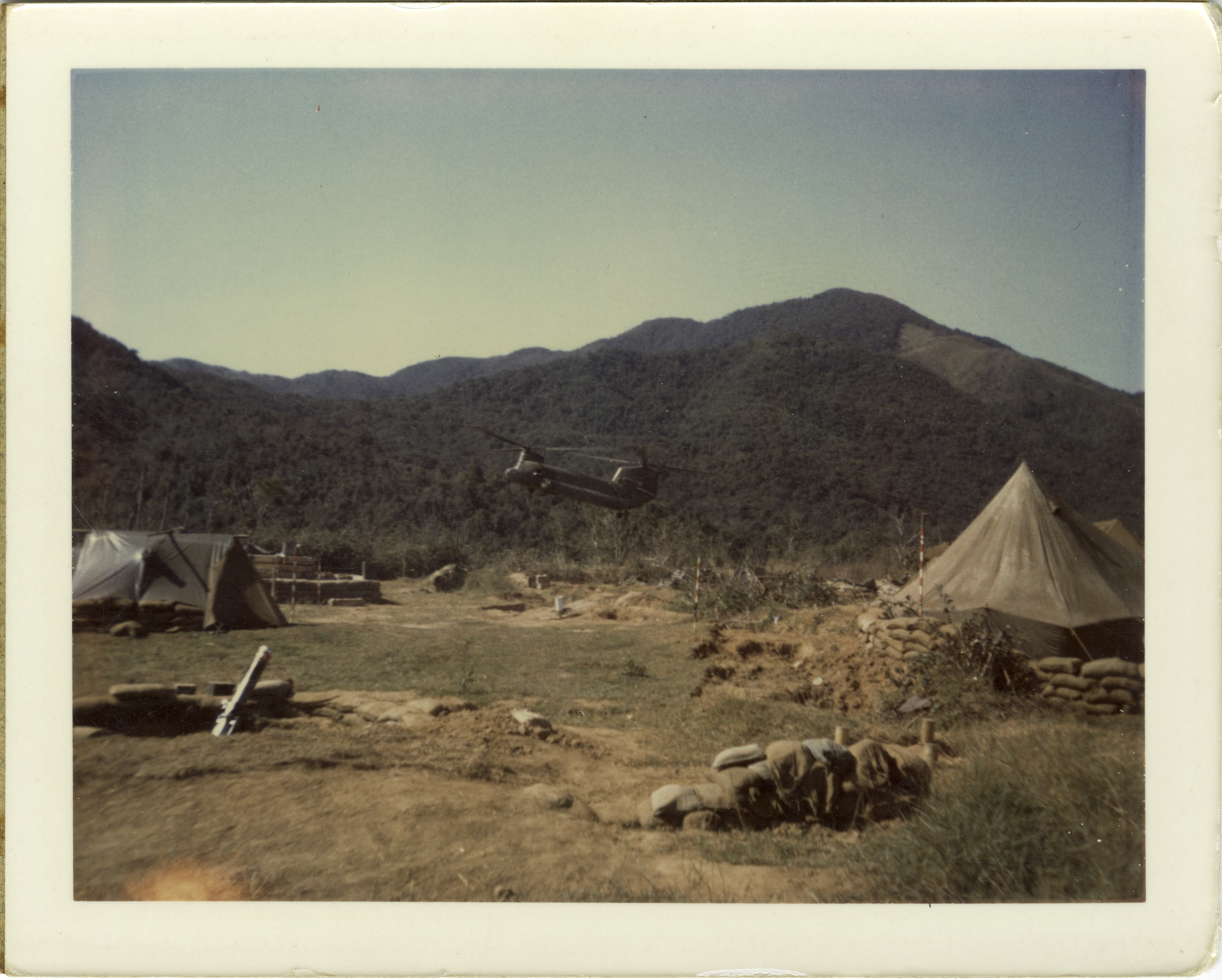A military base with tents, a helicopter, and mountains in the background.