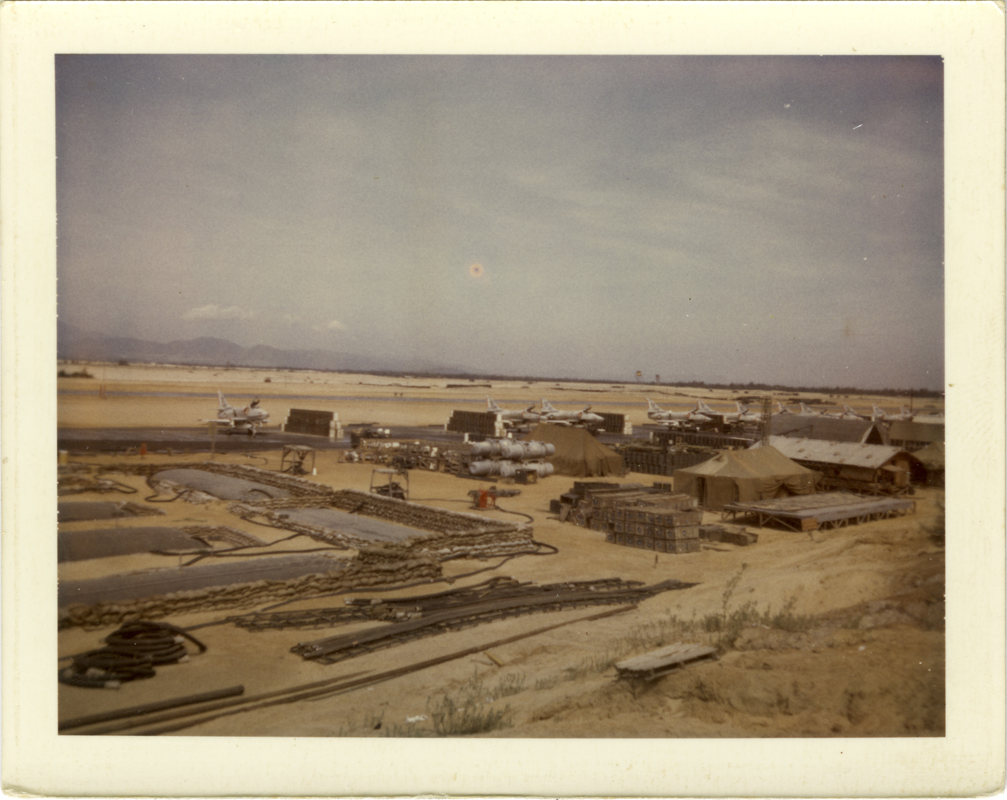 An air base surrounded by flat tan landscape and mountains in the far distance.