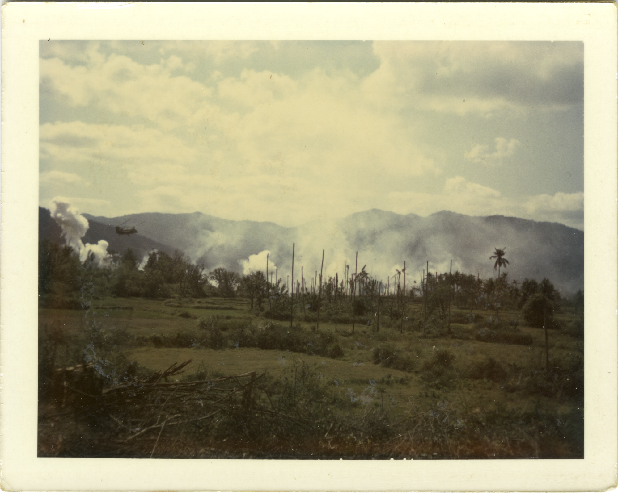 Photos of a green field with trees, smoke in the distance, and mountains beyond