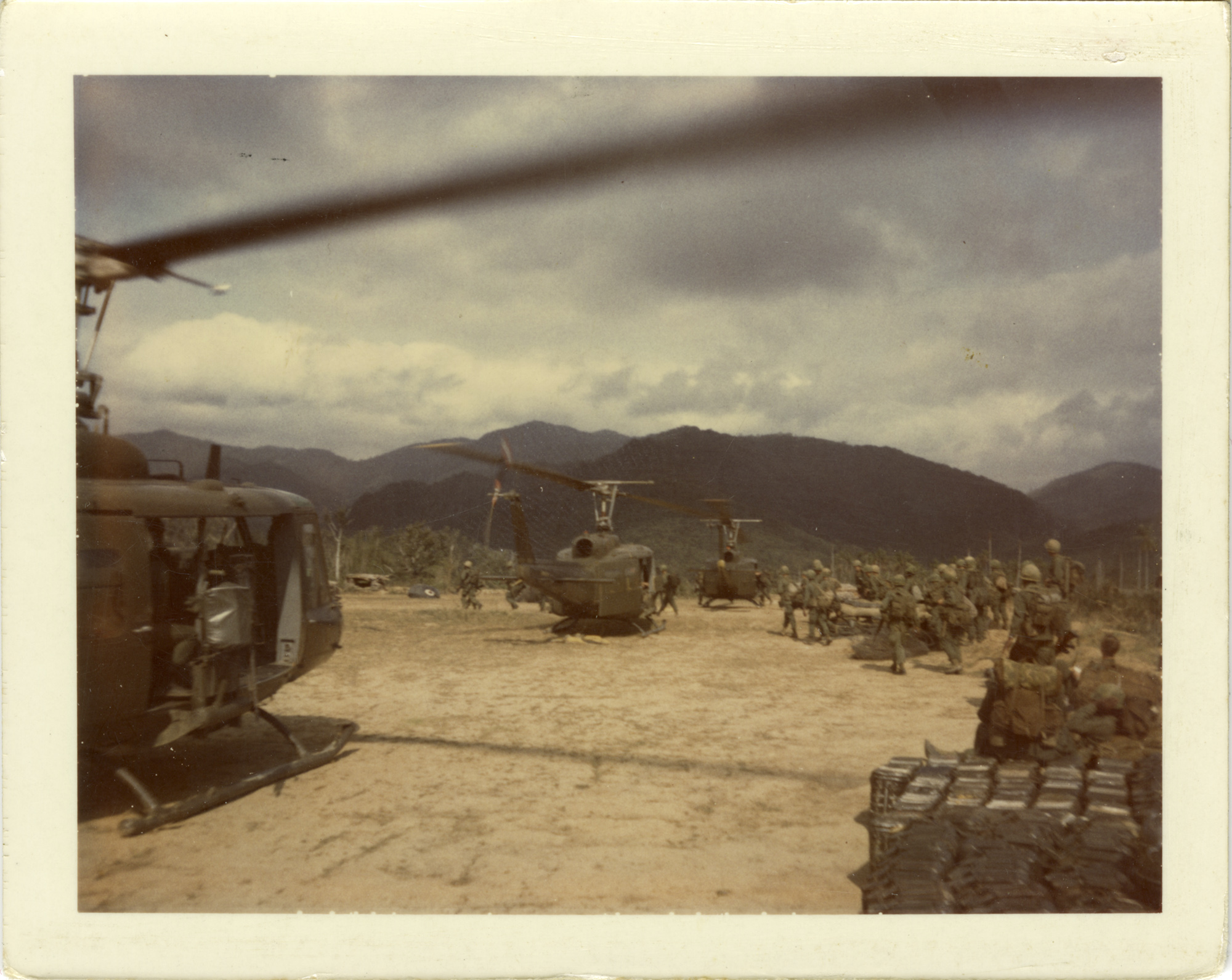 A group of military helicopters stations on the ground with mountains in the distance