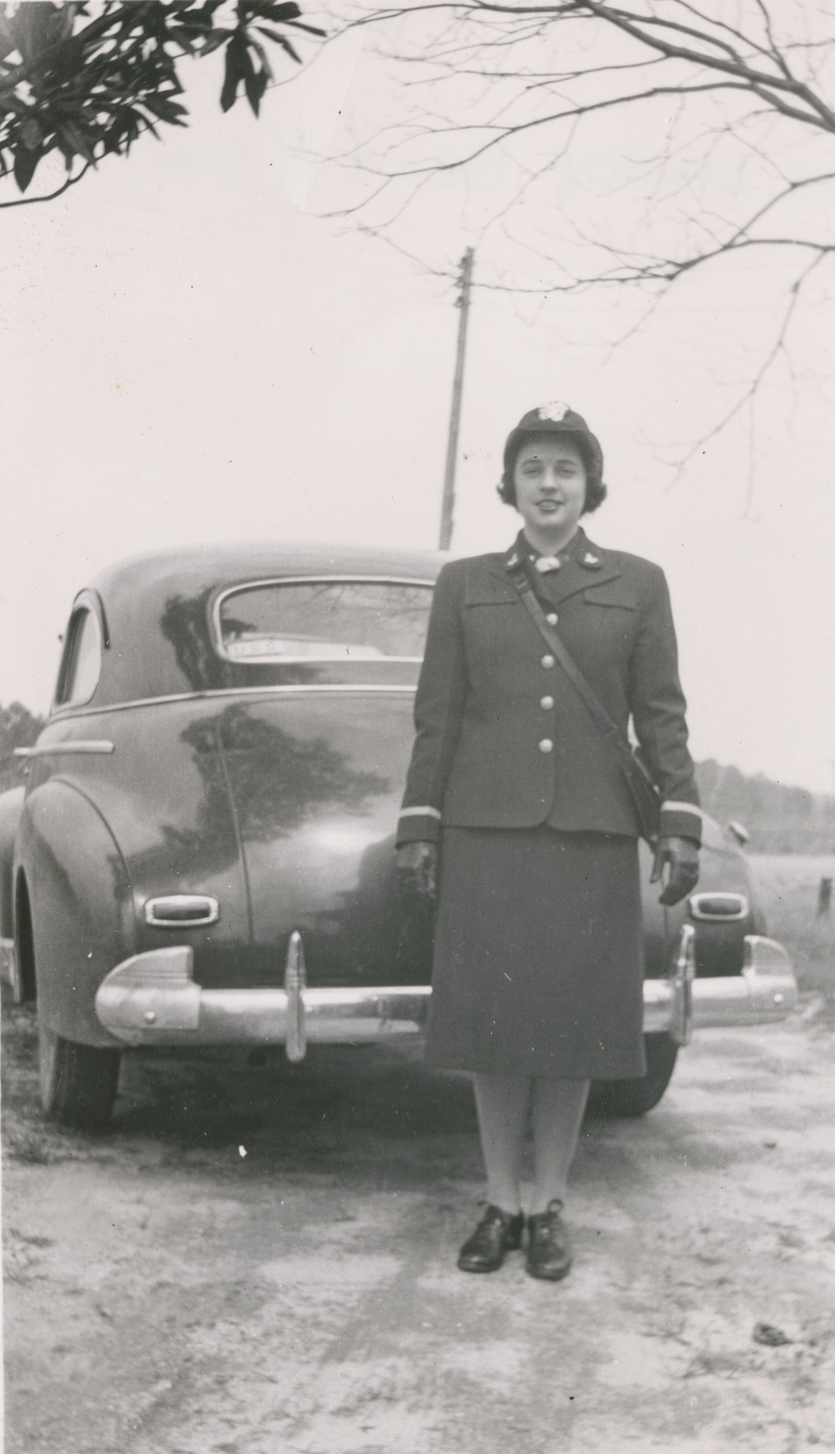 A black and white photograph of Nancy Bailey Cogsdale in her WAVES uniform standing in front of a car
