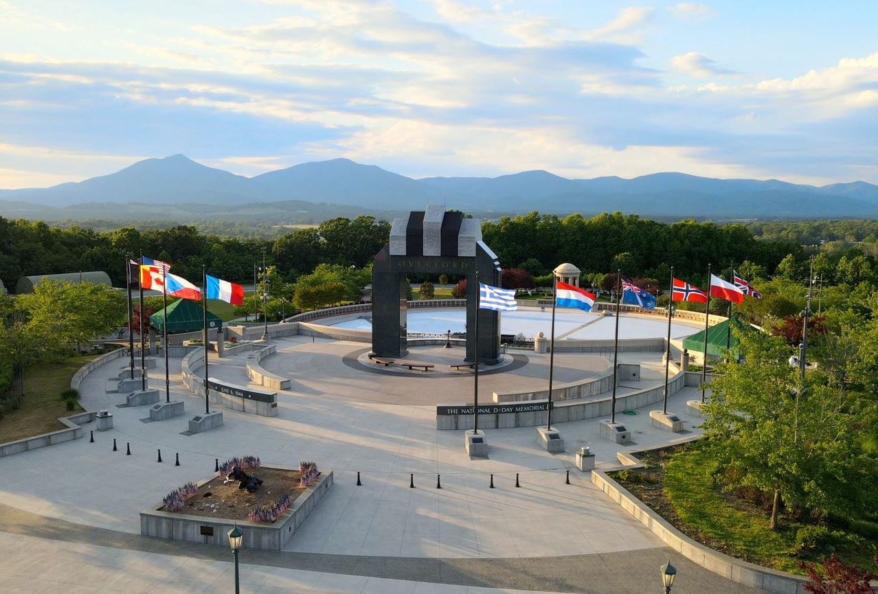A wide circular plaza with a dark stone arch in the center and international flags along the perimeter, with a mountain range visible in the background