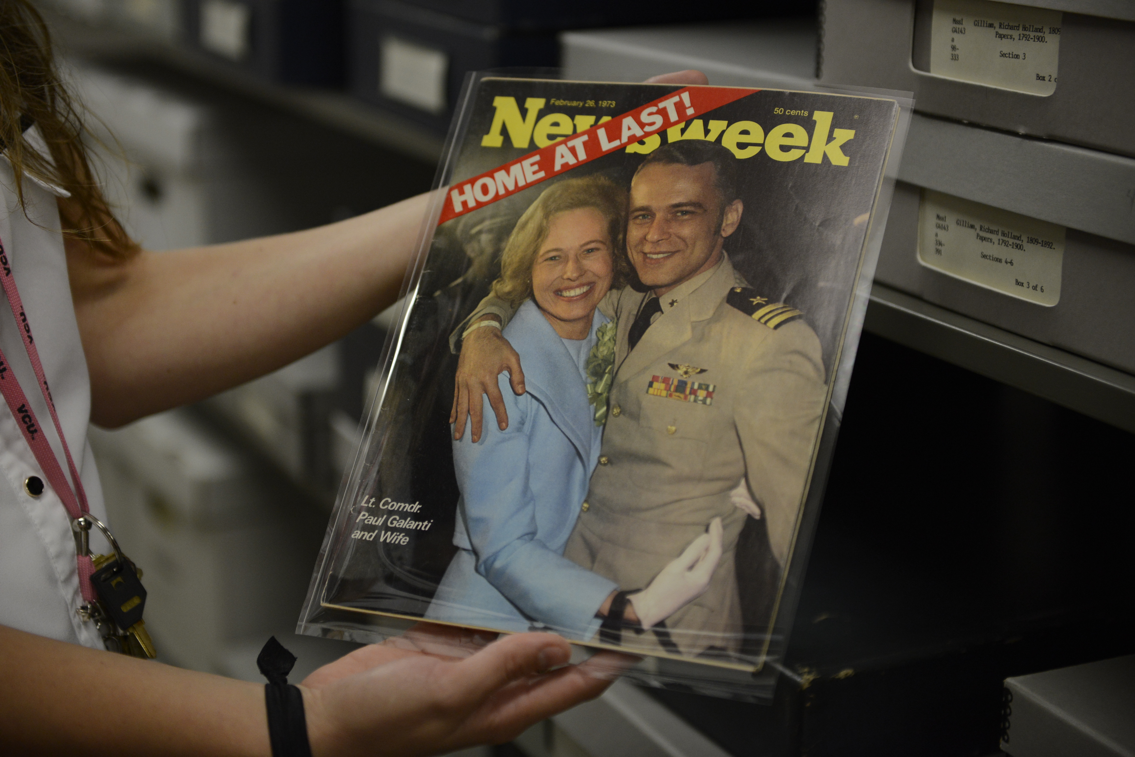 An archivist holds a historic issue of Newsweek magazine with the headline Home at Last! and a photo of Phyllis Galanti in a pale blue jacket embracing her husband Paul Galanti in U.S. military uniform