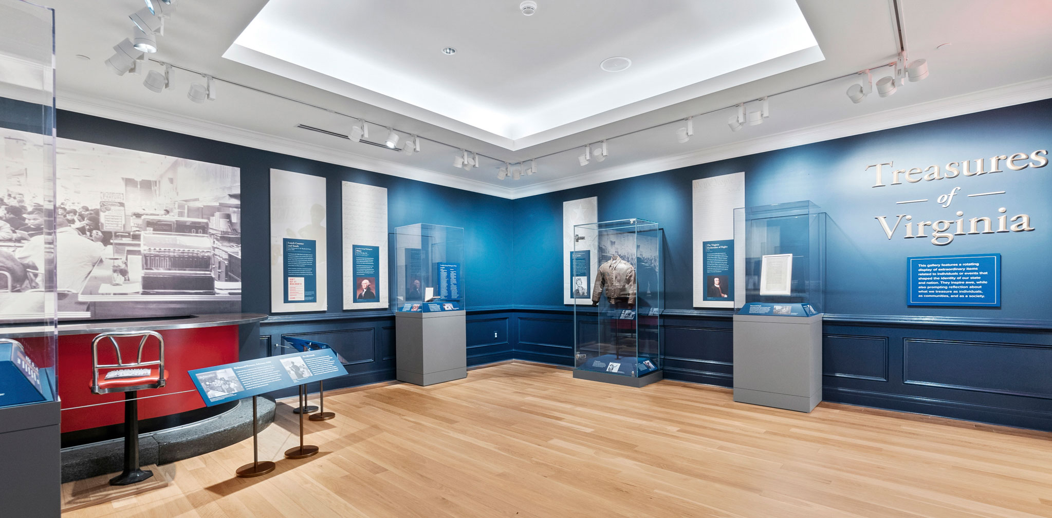 A gallery with blue walls, objects in display cases, and lettering that reads Treasures of Virginia