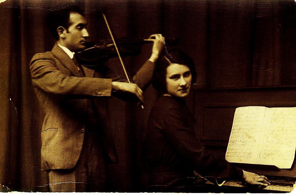 A sepia photo of a man standing and playing a violin and a woman seated and playing a piano