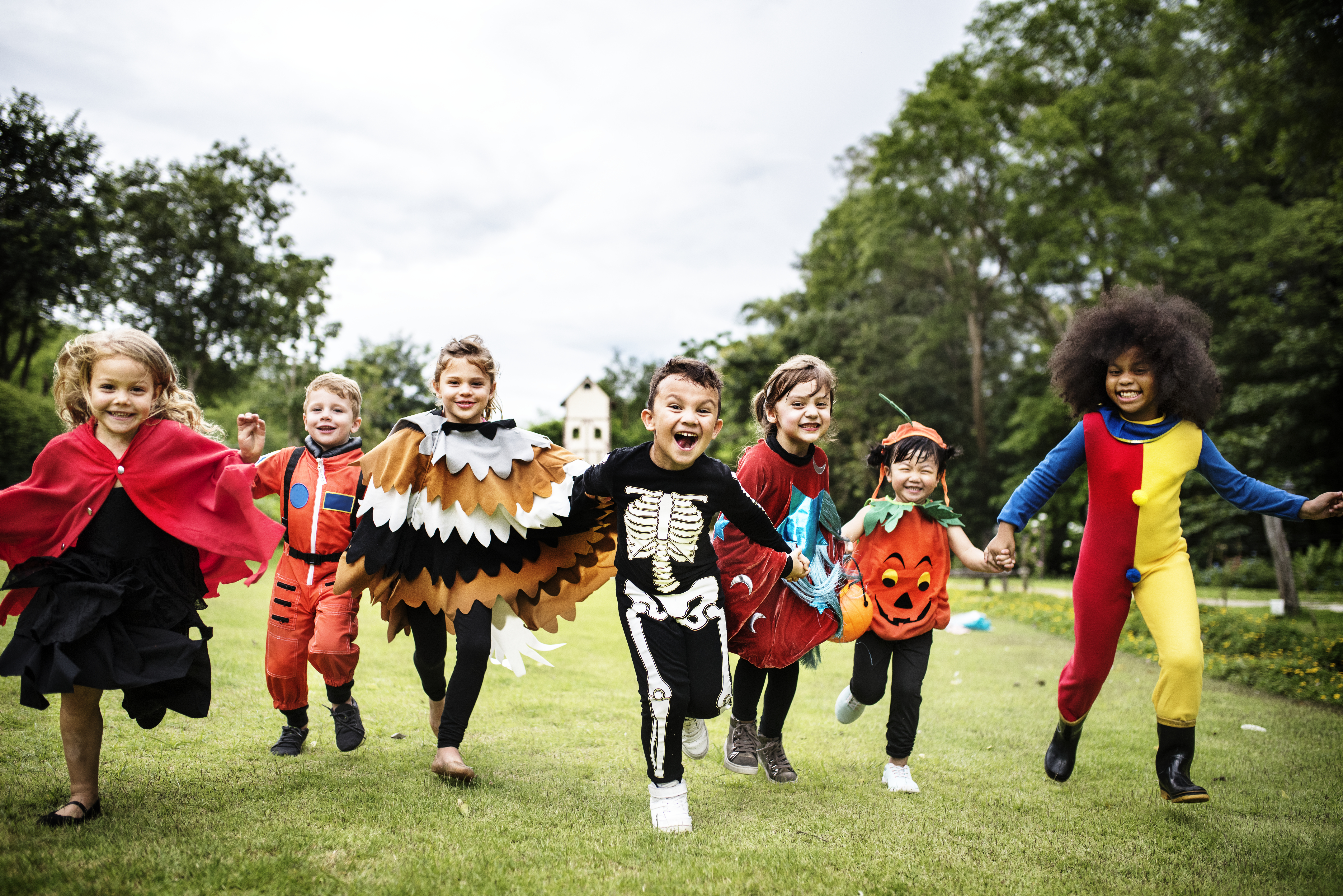 7 kids in various costumes running toward the camera on a grassy field 