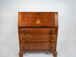 A wood rolltop desk with three drawers and a gold scale symbol embossed on the top