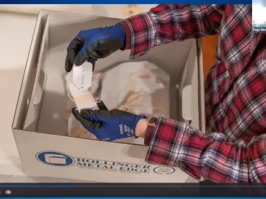 two gloved hands look at a call slip while unpacking a box with a paper-wrapped object
