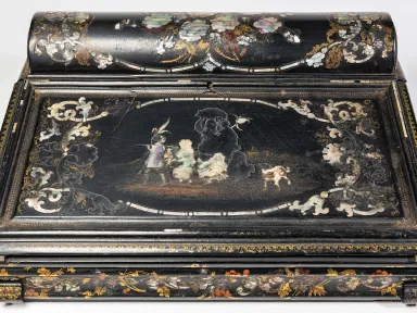 A top-down view of a small black-laquered writing desk with pearl inlaid in a floral motif.