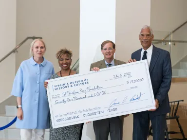 Four people stand holding a giant check