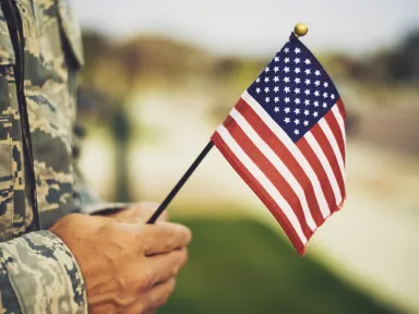 person in military camoflauge uniform holding an american flag