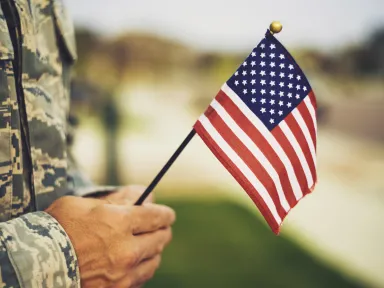 Military member with flag person in military camoflauge uniform holding an american flag