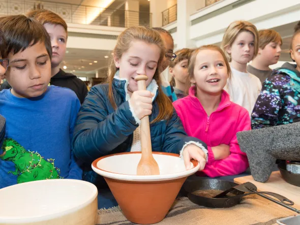 Children contribute to a chocolate making demo by stirring with a bowl and wooden spoon