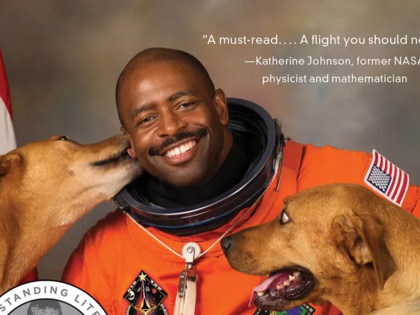 A photo of Leland Melvin in his orange spacesuit with his two dogs