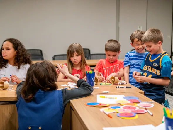 Children work on crafts at table with a teacher. 