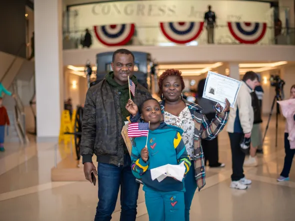 Family stands in the VMHC Musuem Atrium with American flags and Naturalization Certificates. 