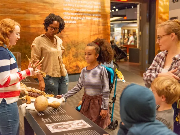Adults and children gather around a table with historical artifacts