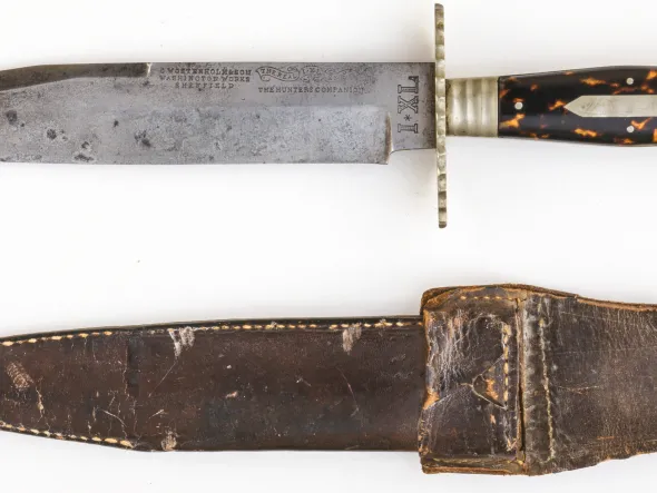 Bowie knife and sheath. Clip-point steel blade. he knife bears the following mark on left side of blade: "G WOSTENHOLM & SON / WASHINGTON WORKS / SHEFFIELD" (at left) and "THE REAL I XL KNIFE / THE HUNTERS COMPANION" (at right). The text of "THE REAL / I XL / KNIFE" is split between three small ribands. The knife also bears the following mark at the left ricasso: "I*XL". 