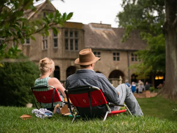 Two people sit in lawn chairs facing a historic Tudor mansions