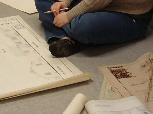 A person sits on the floor surrounded by architectural drawings