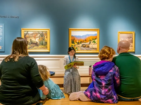 An educator reads a historical story to a family seated in a gallery