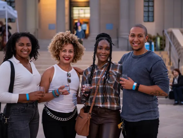 A photo of four smiling people standing in front of the museum holding wine glasses