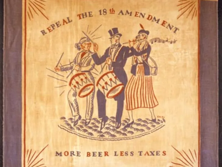 "Repeal the 18th Amendment/ More Beer Less Taxes" scarf, 1920s A square scarf with a blue border and an illustration of three people in the center, two of whom play handheld drums and 1 of whom plays a flute. Words read "Repeal the 18th Amendment: More Beer Less Taxes"