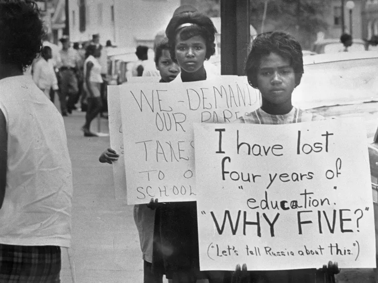 Two Black female students protesting school closures by marching with posters