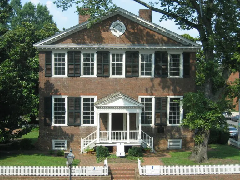 A two-story brick colonial-style house with white window trim and brown shutters