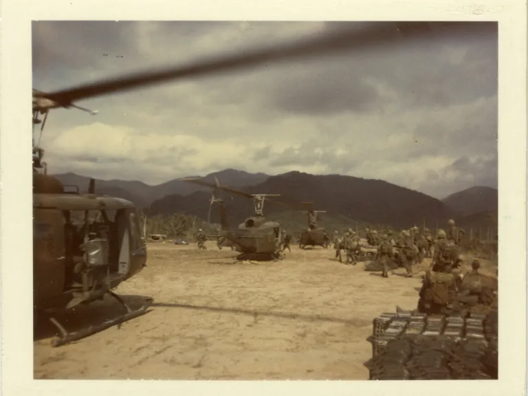 A group of military helicopters stations on the ground with mountains in the distance