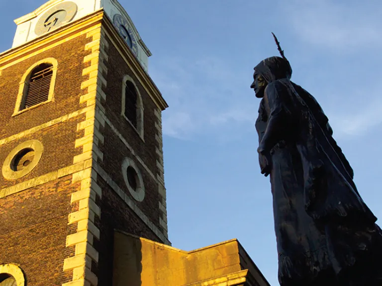 A statue of Pocahontas next to a tall brick tower