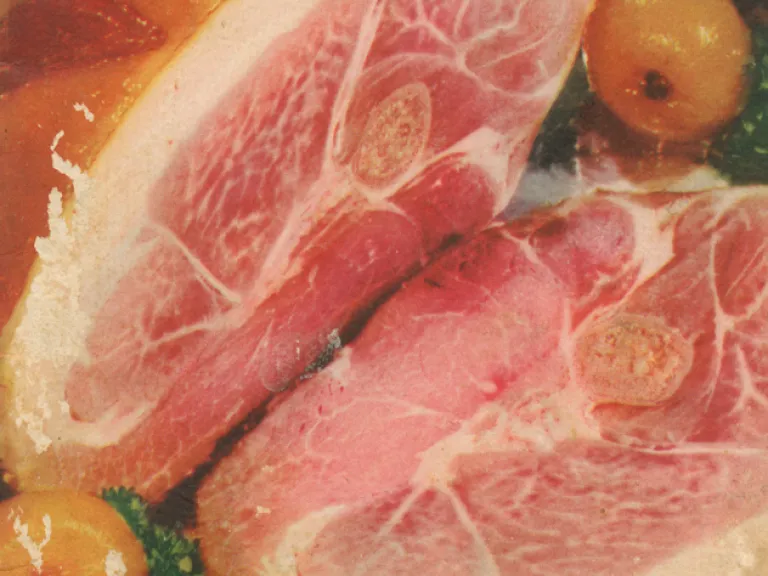 A color photograph of a sliced country ham, with yellow tomatoes on the side
