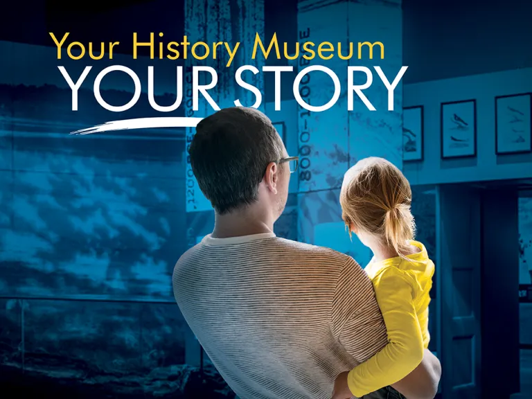 A parent holds a child as they look into a museum exhibition. Above their heads are the words: Your History Museum, Your Story
