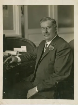 James E. Crass A sepia photograph of James E. Crass in a suit sitting at a roll-top desk