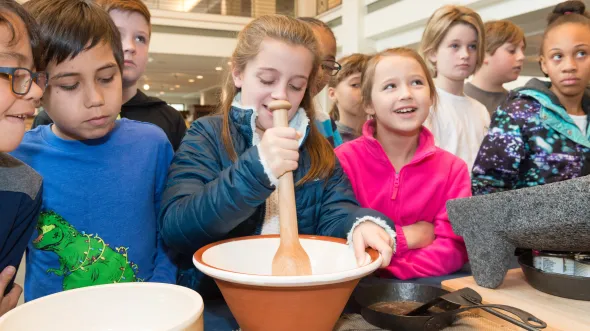 Children contribute to a chocolate making demo by stirring with a bowl and wooden spoon