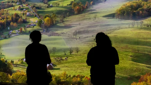 Two silhouetted people view a large screen projection of rolling hillsides.