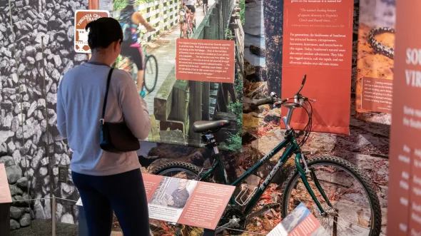 A woman looks at a museum display including a bicycle and photographs of bike trails