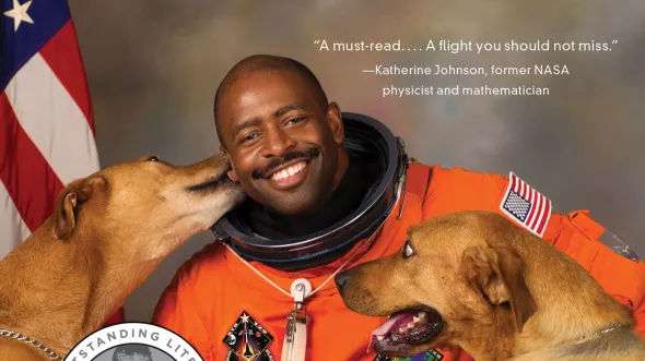 A photo of Leland Melvin in his orange spacesuit with his two dogs